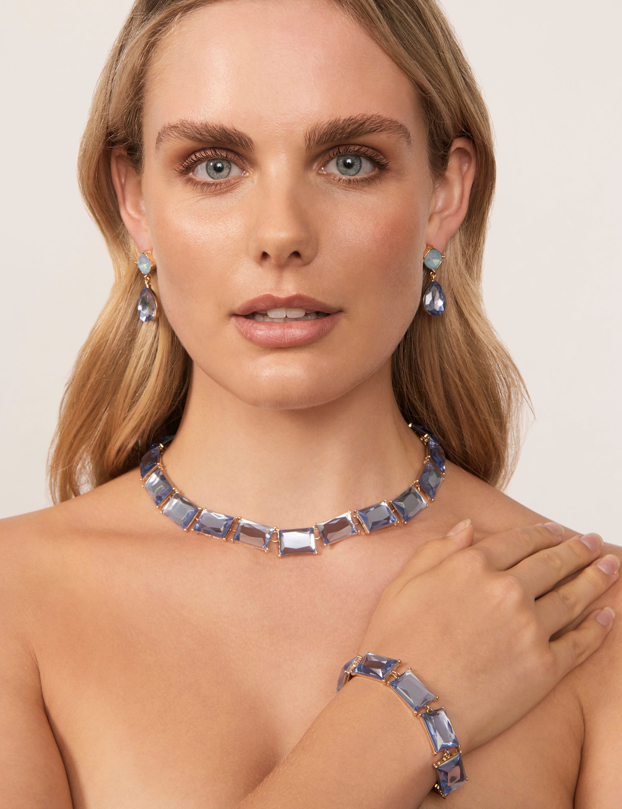 Bridgerton inspired fashion - A woman wearing a blue stone necklace, matching bracelet, and blue teardrop earrings.